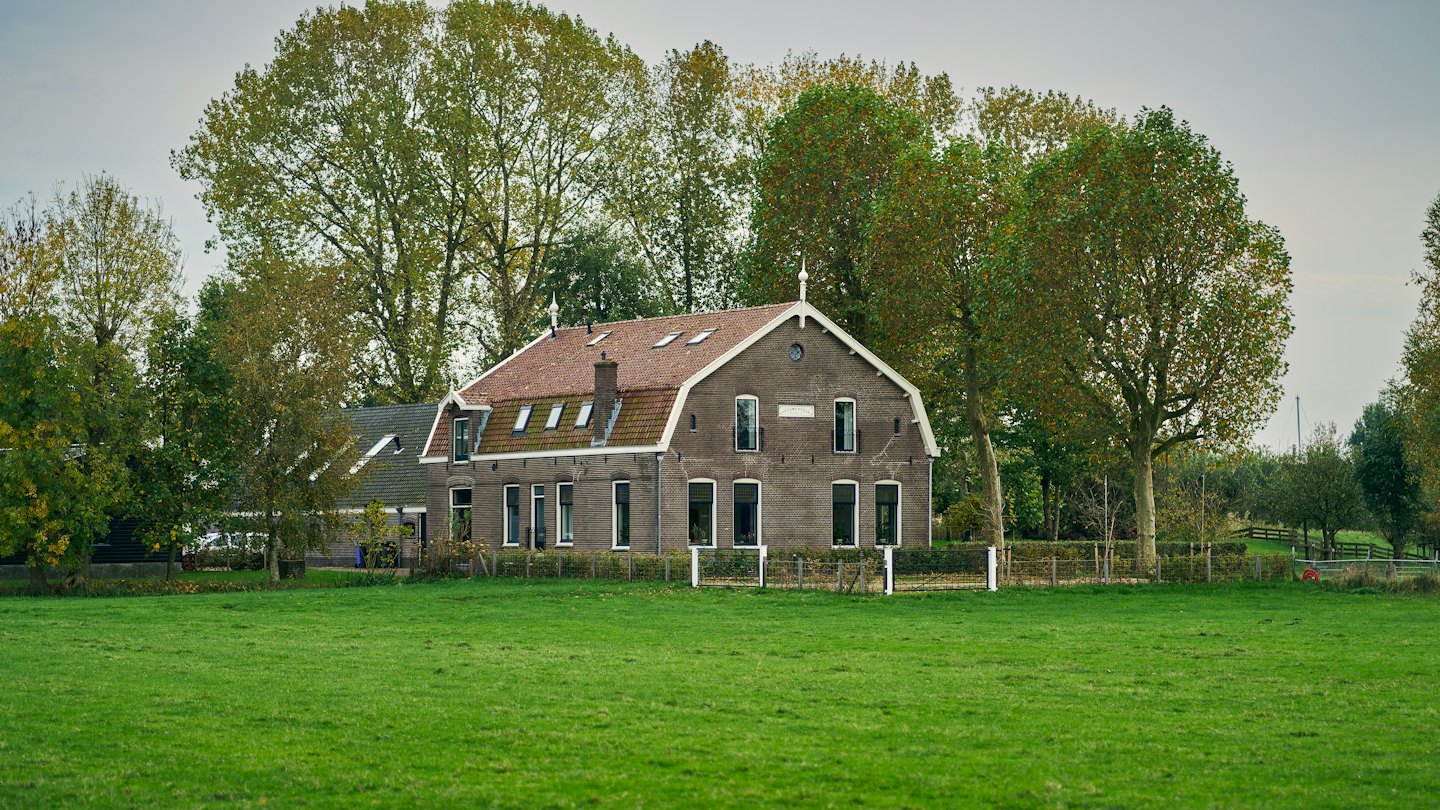 Een traditionele bakstenen boerderij met een rood dak staat in een veld.
