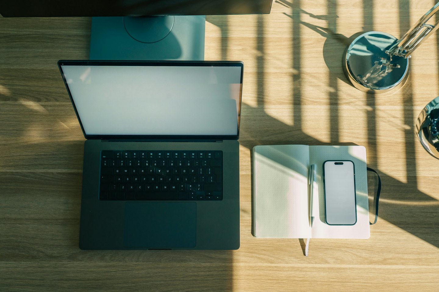 Laptop, notitieboek en smartphone op een houten bureau.