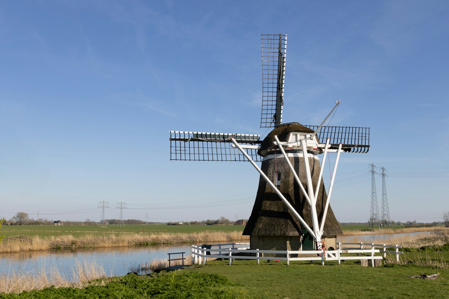 Traditionele Nederlandse windmolen op gras naast een kanaal.